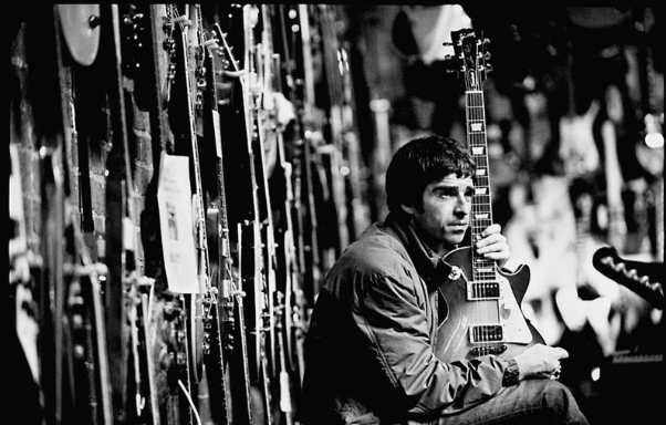 Black and white photo of rock musician Noel Gallagher with a guitar.