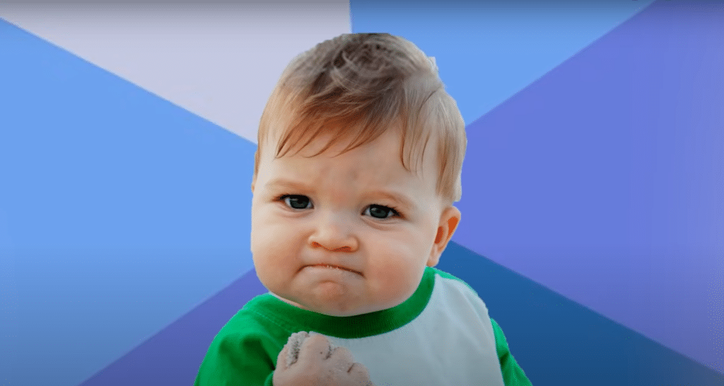 Little chubby baby, also known as Success Kid, clenching a fistful of sand with a determined facial expression.