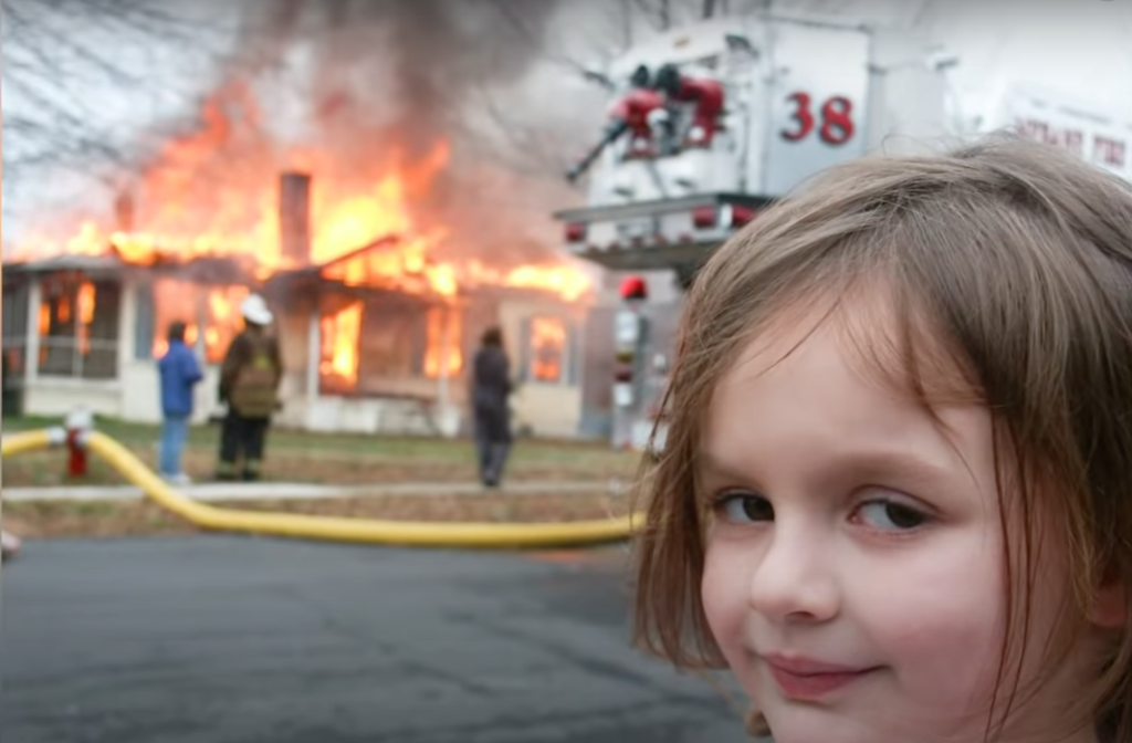The image of Zoë Roth, known as the "Disaster Girl." She stands in front of a burning house, smiling in a sinister way. 