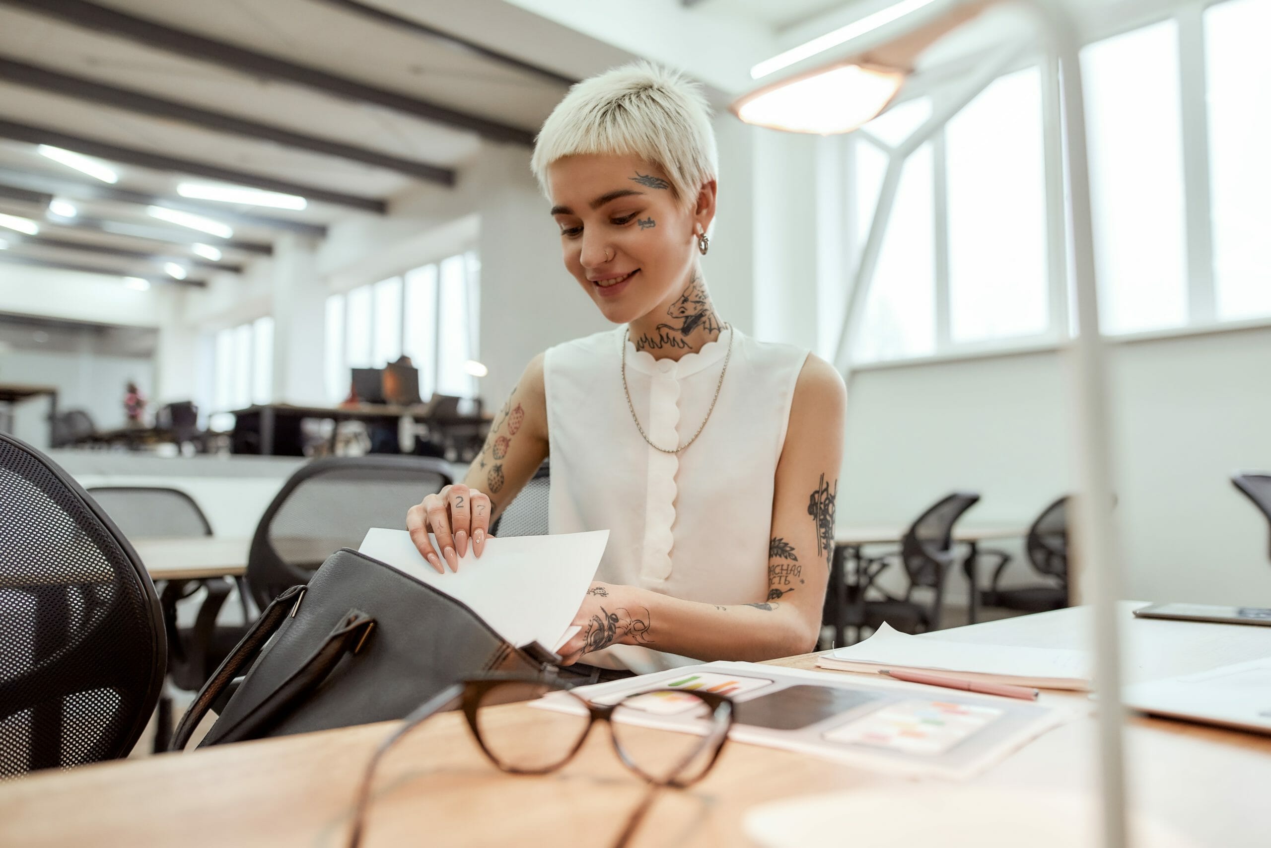 White woman with visible tattoos sitting at an office desk