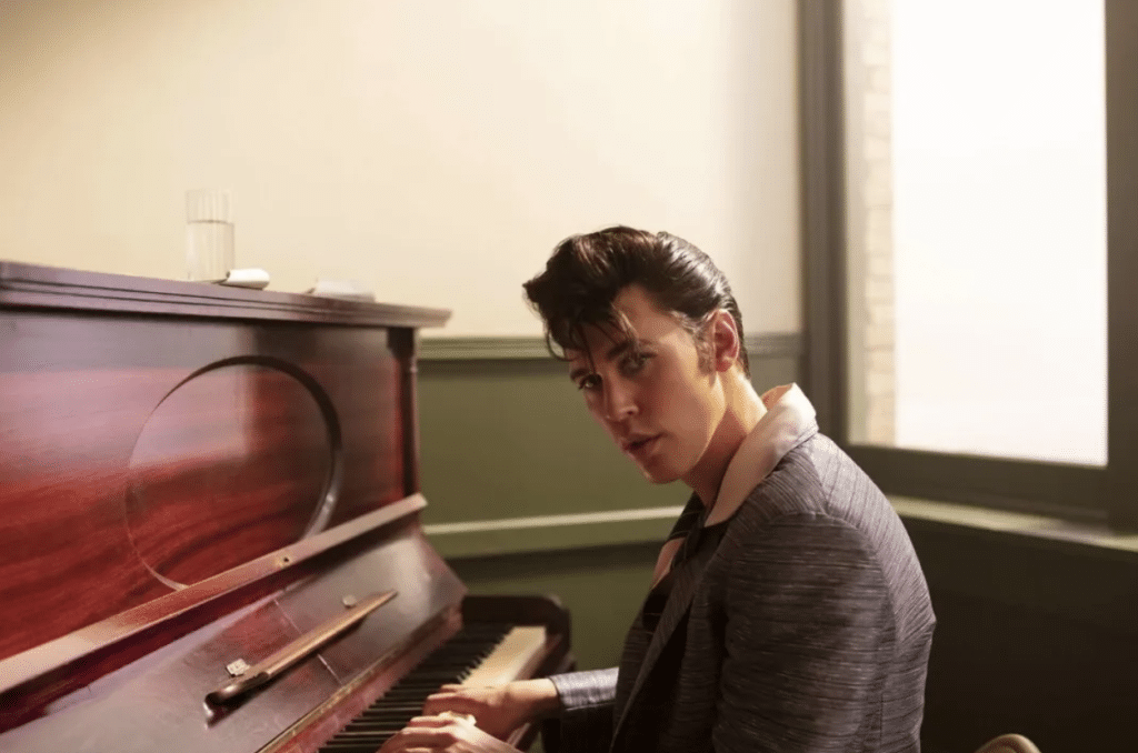 Elvis (Austin Butler) plays the piano and looks into the camera.