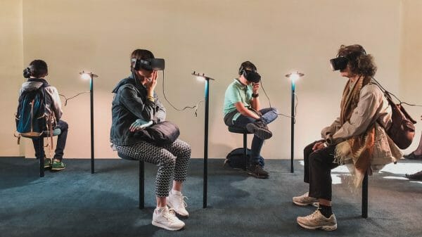 By Unsplash user Lucrezia Carnelos. Many people with VR headsets sit around in a room.