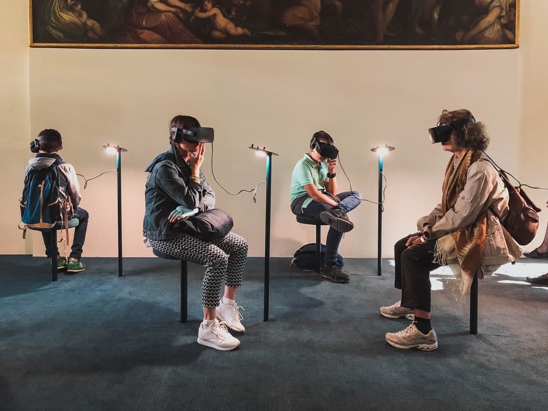 By Unsplash user Lucrezia Carnelos. Many people with VR headsets sit around in a room.