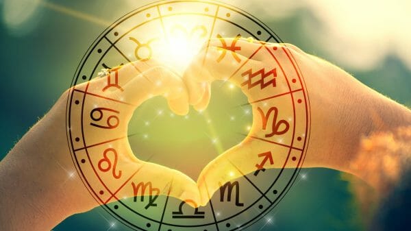 Two hands making a heart with a zodiac wheel surrounding it