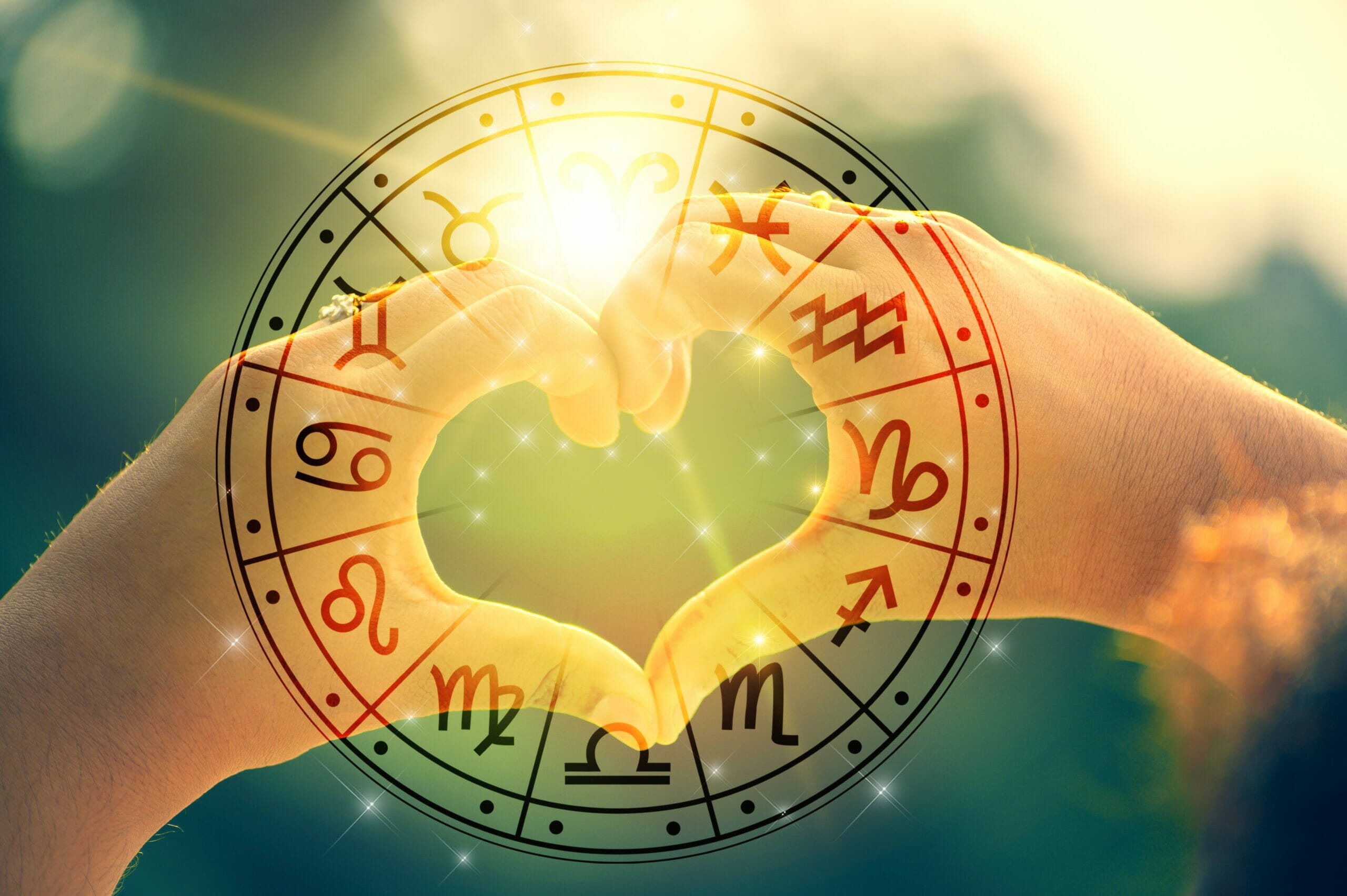 Two hands making a heart with a zodiac wheel surrounding it