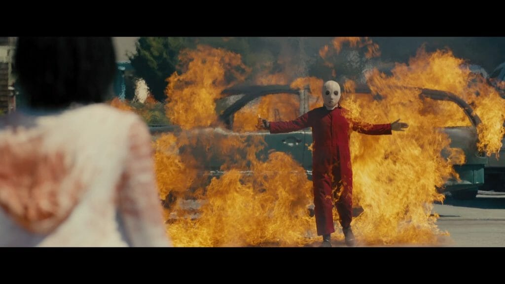 Screenshot from Jordan Peele's Us showing a young boy with a white mask standing in a fire