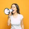 Woman screaming into a megaphone against a yellow background