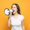 Woman screaming into a megaphone against a yellow background