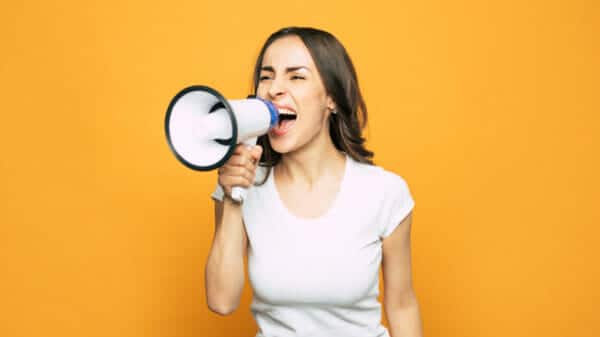 Woman screaming into a megaphone against a yellow background