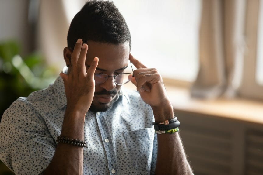Black man with glasses putting fingers on temples looking stressed