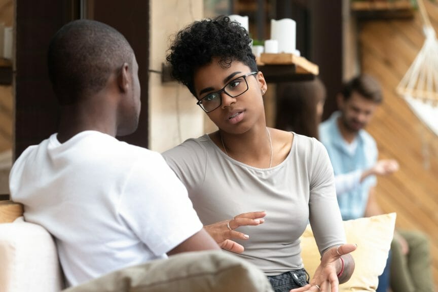 Black woman with glasses talking seriously to a Black man on a sofa