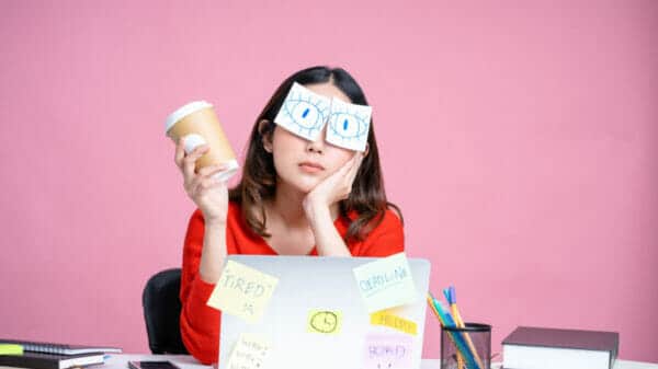 A woman holding a coffee cup bored with her numerous duties at work