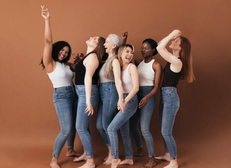 A group of women dancing together in matching outfits and in front of a brown backdrop.