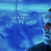 Jake Sully (Sam Worthington) looks away from the camera with his avatar behind him in a tank