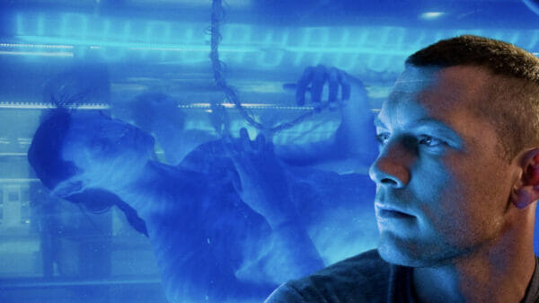 Jake Sully (Sam Worthington) looks away from the camera with his avatar behind him in a tank