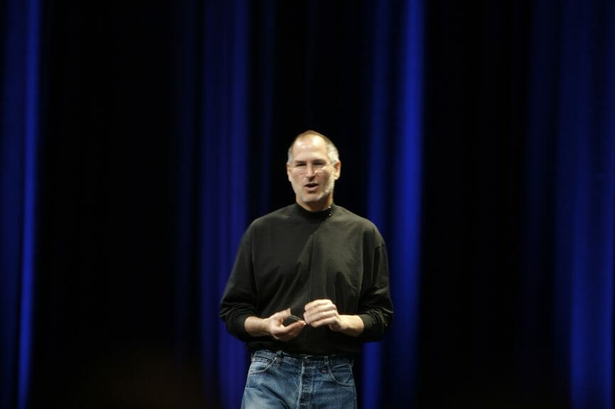 Steve Jobs wearing jeans and black turtleneck at apple conference.