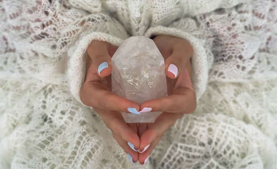 Hands with pastel painted nails holding a clear quartz crystal