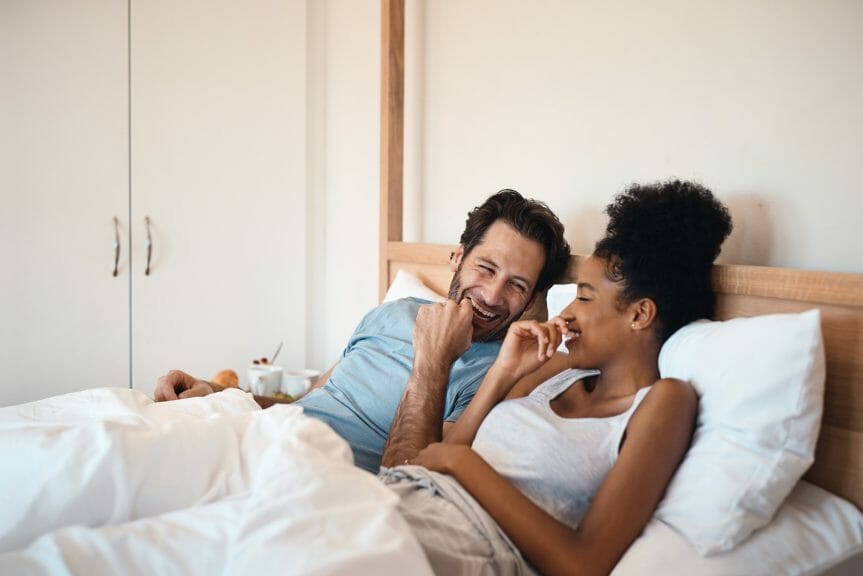 Interracial couple laughing together in bed enjoying an intimate moment together