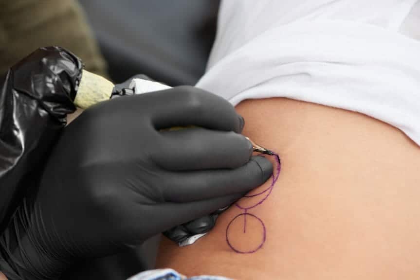 Artist creating minimalist tattoo on client with fine lines and circles