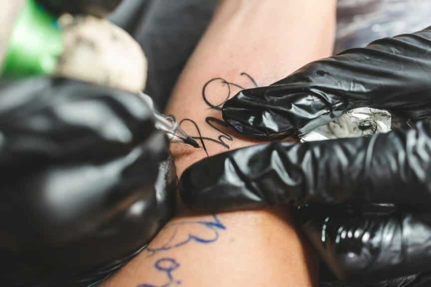 Artist creating fine line script style tattoo on client