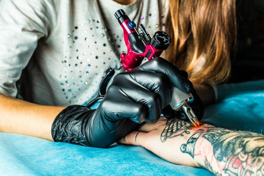 Artist tattooing client on the back of hand