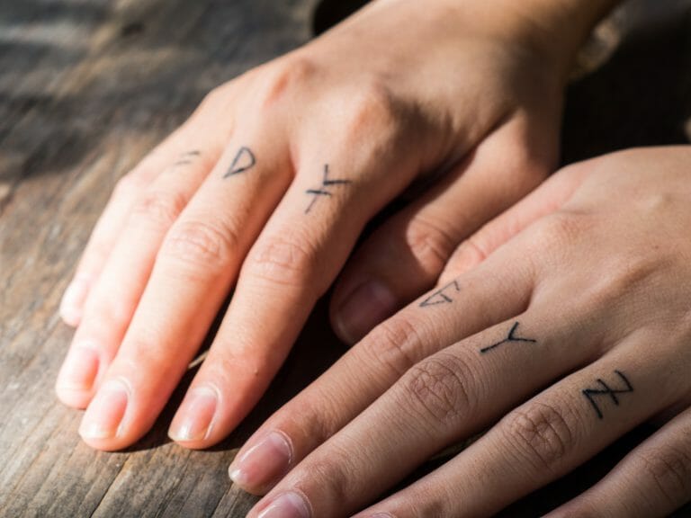 Up close hands with black rune tattoos on fingers