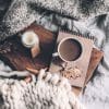 Candle, hot drink, notebook, and knitting on a cozy bedspread