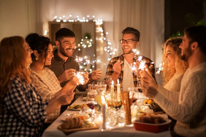 Smiling friends sitting at a festive dinner table holding sparklers