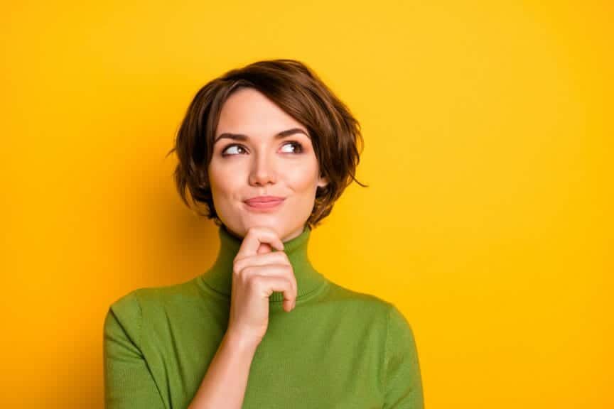 Woman thinking with hand up to her chin with green shirt and yellow background