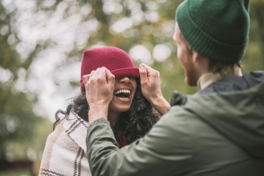 Playful, laughing couple where the man is pulling a beanie hat over the womans face.