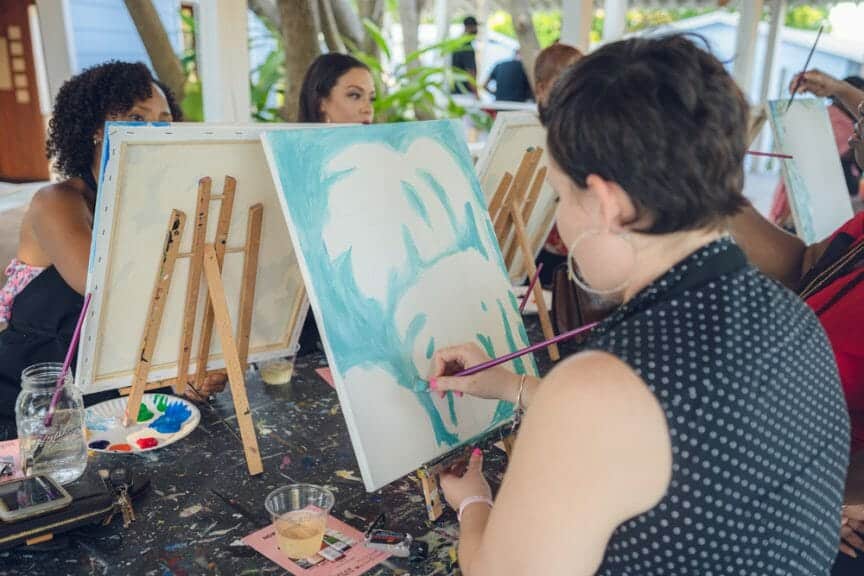 College students at paint-and-sip class, subject is painting with light blue on canvas