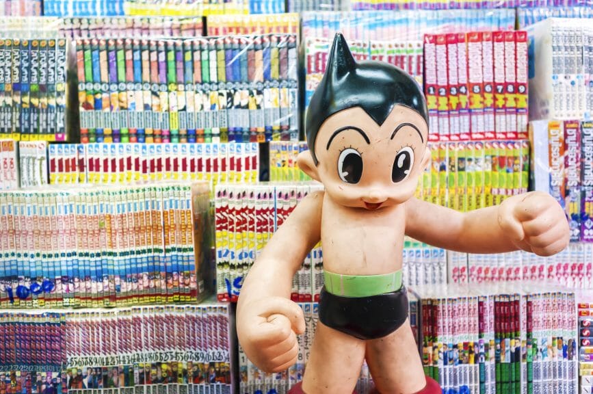 An Astro Boy statue in front of stacks of manga. 