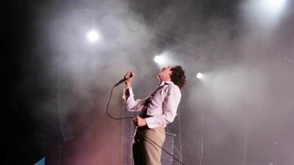 Matty Healy singing into microphone on a smoky stage