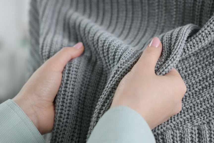 Person touching grey knitted sweater.