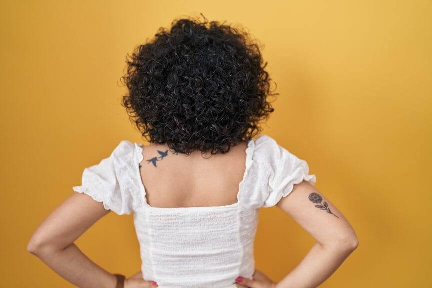 Woman with short curly hair facing away from the camera with a yellow background.
