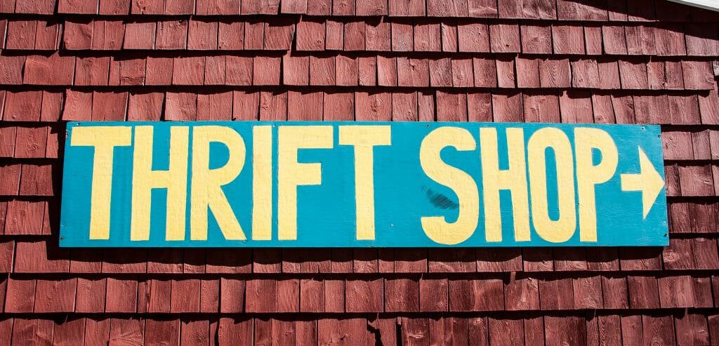 Blue sign with yellow letters that reads "thrift shop" with an arrow.