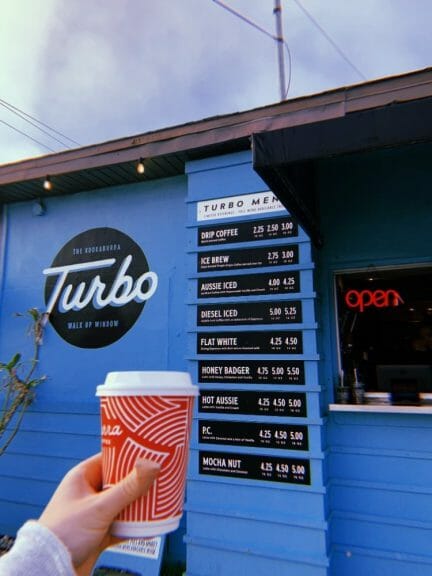 A To-Go coffee cup is held in front of The Kookaburra Turbo Walk Up Window, a local spot in St. Augustine, Florida.
