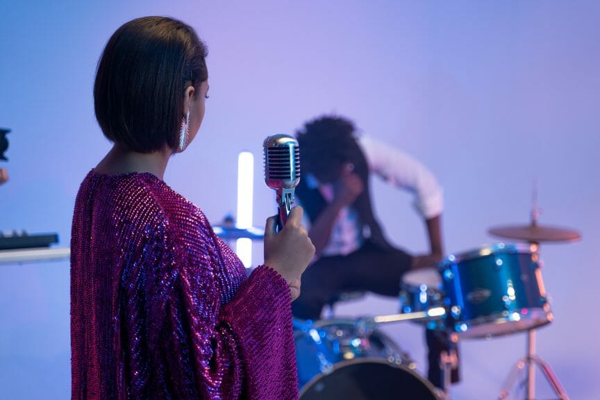Woman holding a microphone and looking behind her at drummer.