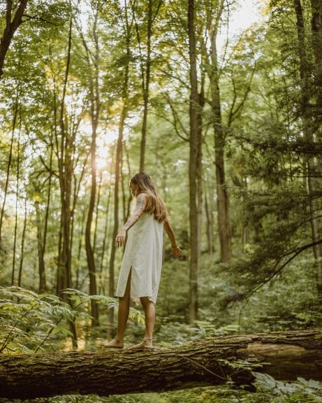 Girl in white dress balances on log in forest