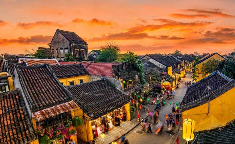 City of Hoi An in Vietnam, featuring close together buildings with street lights hanging from the rooftops and people walking around.