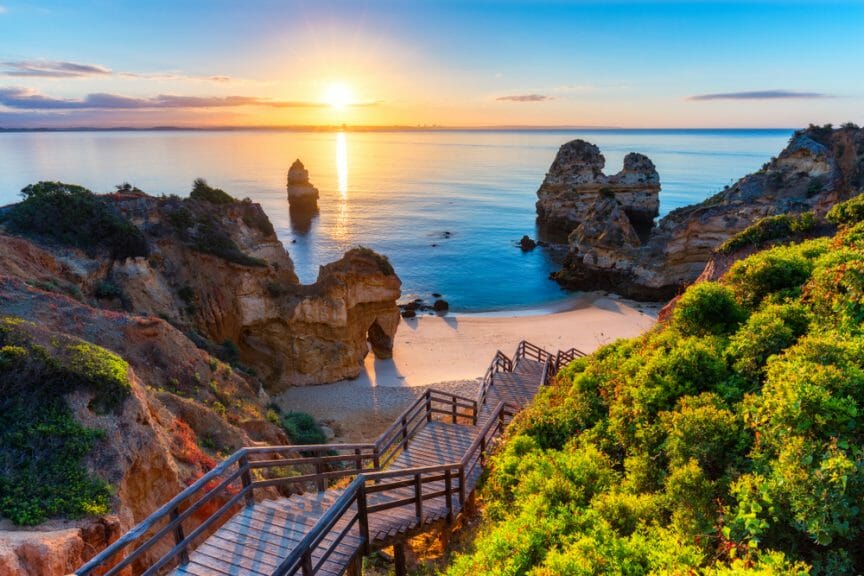 Camilo beach travel destination in Portugal. The beach is surrounded by cliffs and trees with a bridge leading to the shore. 