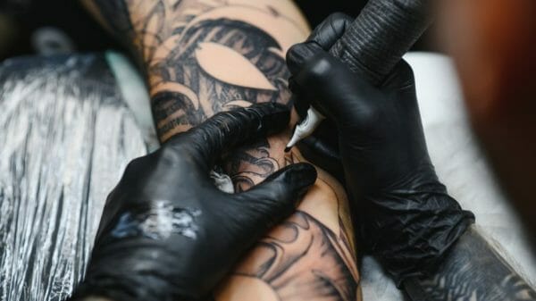 Tattoo artist working on someone's forearm.