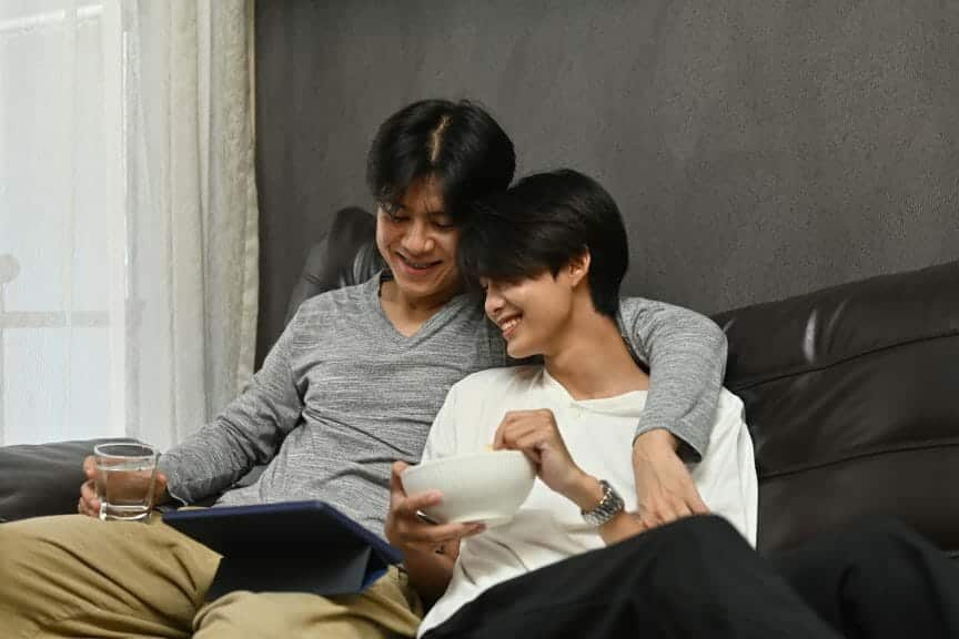 A same sex couple using a tablet while hugging.