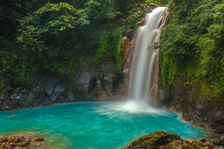 Rio Celeste Waterfall travel destination. Waterfall falling into a clear blue pool surrounded by trees.