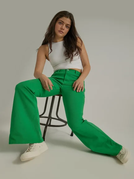 Woman sitting on stool facing camera with green pants.