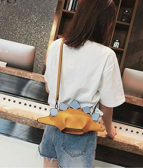 Woman facing countertop with yellow and blue dinosaur purse over her shoulder.