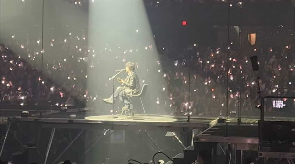 Agust D sitting on a chair playing the guitar.