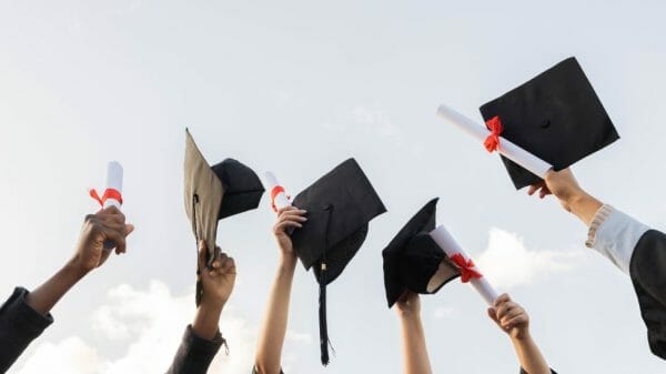 Graduates hold their caps and diplomas in the sky.