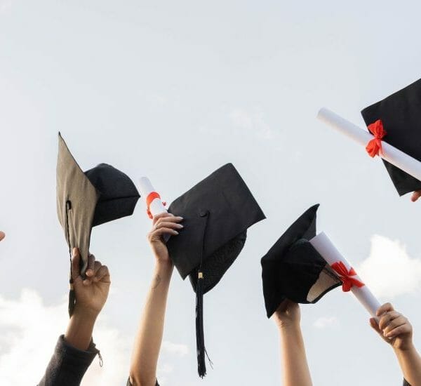 Graduates hold their caps and diplomas in the sky.