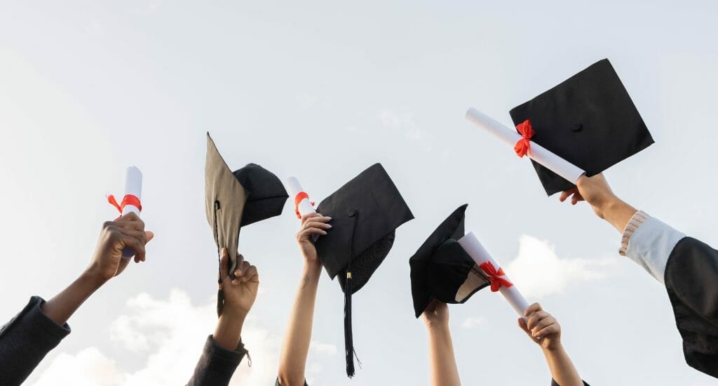 Graduates hold their caps and diplomas in the sky.